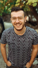 Portrait of smiling young man with hands in pockets standing outdoors