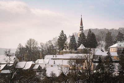 Trees and church and buildings covered with snow against sky during winter