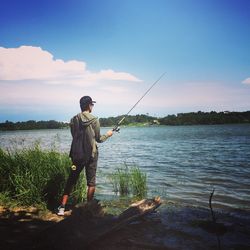 Man fishing on lake against sky