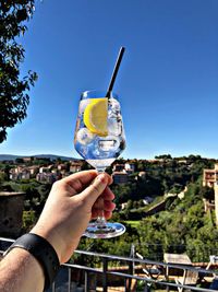 Cropped hand holding drink against clear blue sky