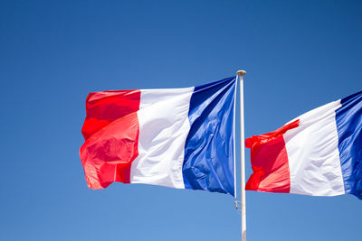 Low angle view of flags against clear blue sky