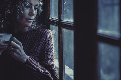 Woman holding coffee cup standing by window