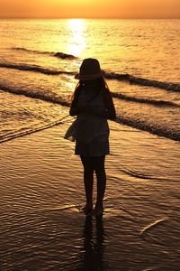 Girl standing on shore at beach during sunset