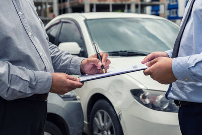 Midsection of man signing on paper with businessman by car