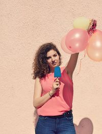 Young woman holding balloons against wall during sunny day