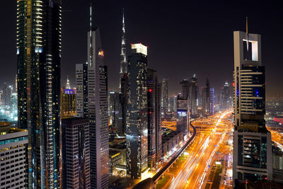 Illuminated city street and buildings against sky at night