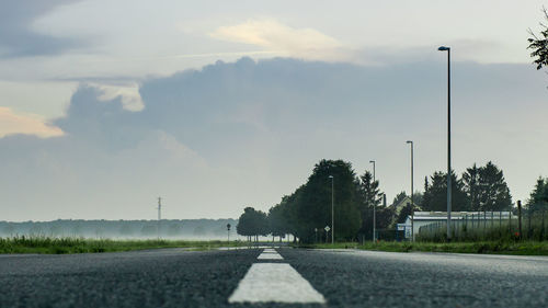 Empty road by trees against sky