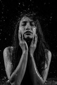 Young woman with water drops against black background