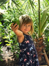 Portrait of girl holding green bell pepper against plants