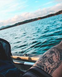 Low section of man relaxing by sea against sky