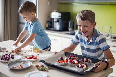 Smiling boy holding desserts in plates in kitchen
