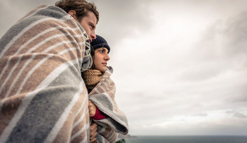 Couple covered with blanket standing against sky