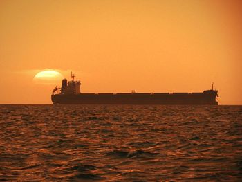 Silhouette ship in sea against orange sky