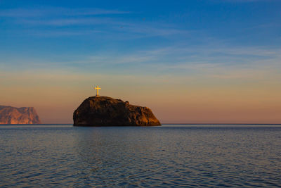Rock formation in sea against sky during sunset
