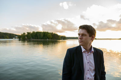 Portrait of young man standing by lake against sky