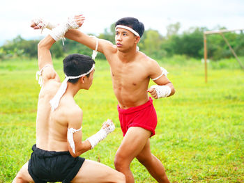 Shirtless young men practicing martial arts on field