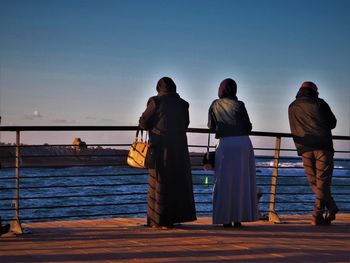 Rear view of people standing by sea against clear sky