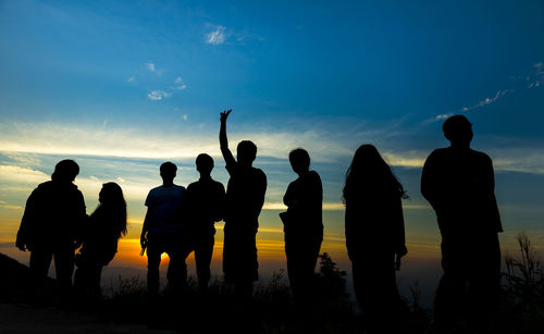 Silhouette people standing by sea against sky during sunset