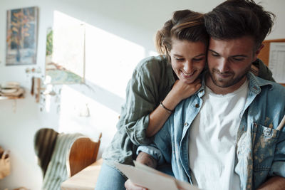 Woman embracing man while looking at document at home