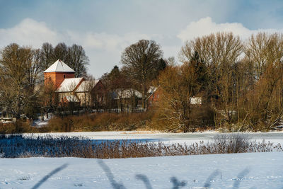 Snow covered field by building against sky