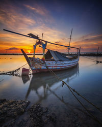 Sailboats moored on sea against sky during sunset