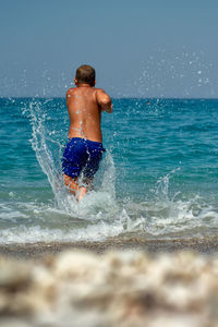 Rear view of shirtless man splashing water in sea