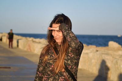 Close-up portrait of young woman standing by beach against sky