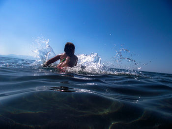 Girl swimming in sea against clear blue sky