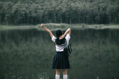 Rear view of woman wearing school uniform while standing against lake