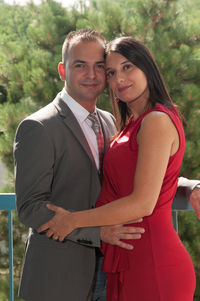 Portrait of man standing with pregnant girlfriend against trees