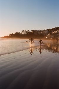 People running on beach against clear sky