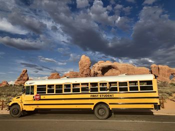 Yellow schoolbus on road against cloudy sky