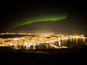Illuminated buildings by sea against sky at night