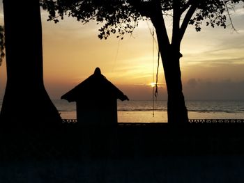 Silhouette built structure by sea against orange sky