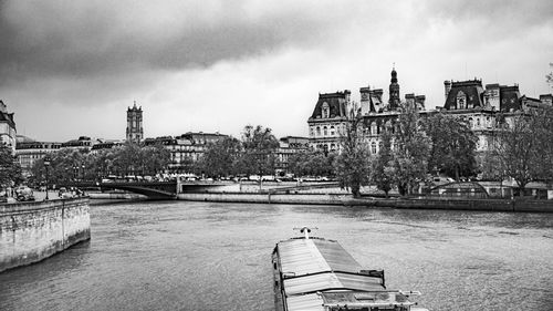 Buildings by river against cloudy sky