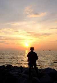 Rear view of silhouette man standing at beach during sunset