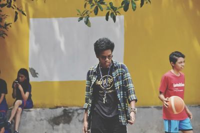 Young man looking away while standing against wall