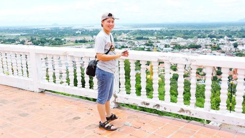 Full length portrait of man standing on railing in city