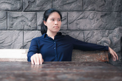 Portrait of young man sitting on table against wall