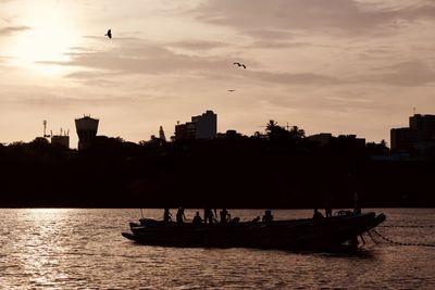 Silhouette boats in river against sky during sunset