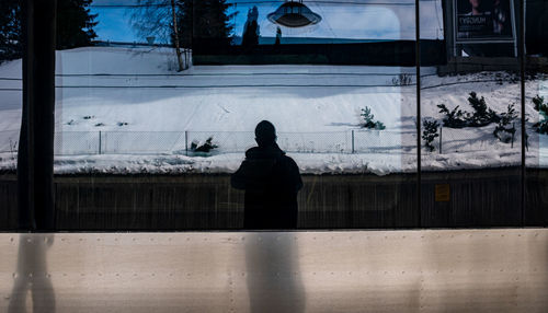 Rear view of silhouette man standing by window