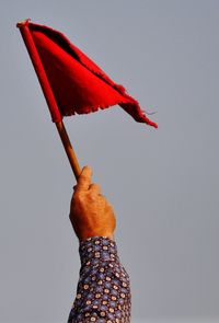 Low angle view of hand holding red flag against clear sky