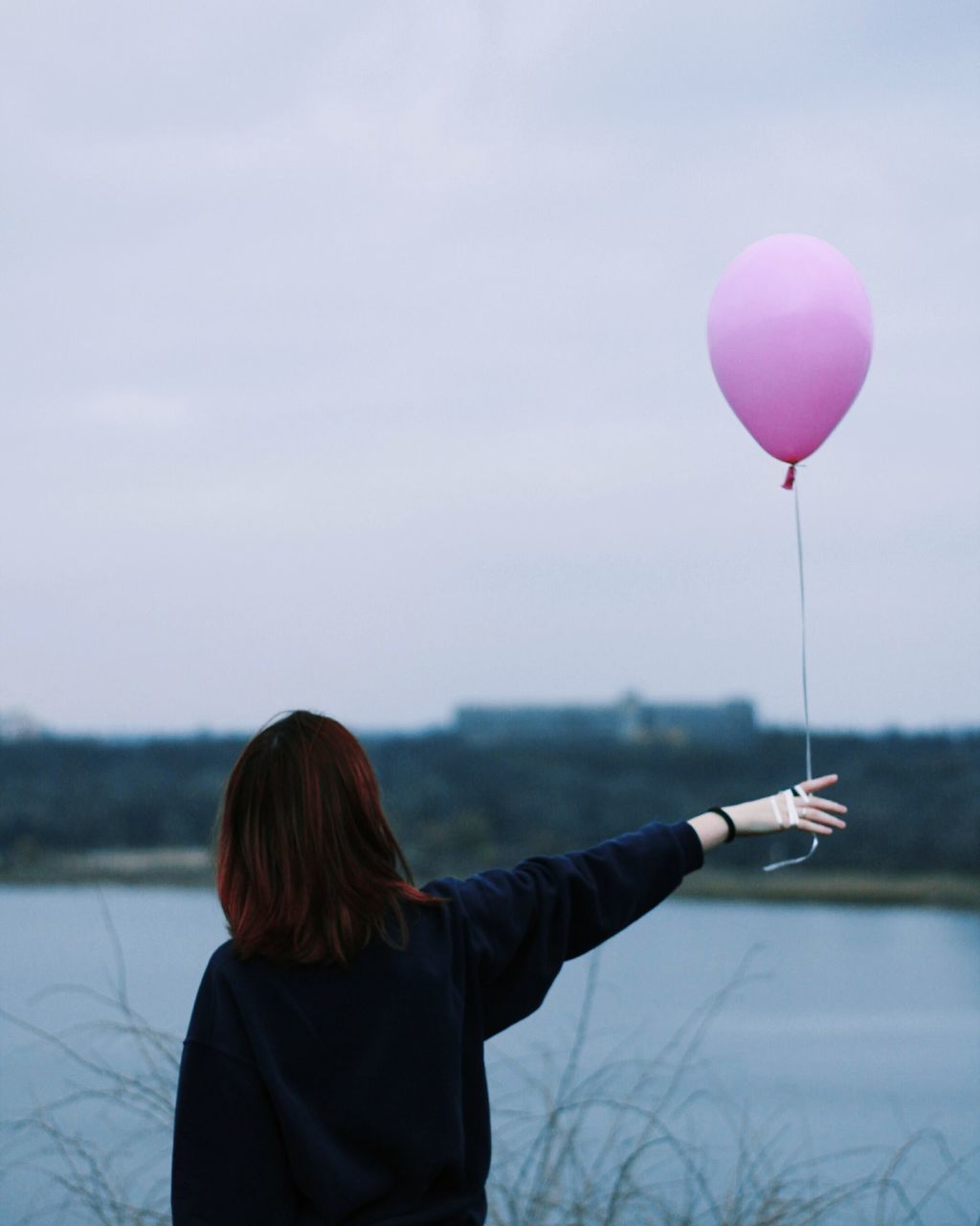 real people, balloon, leisure activity, one person, sky, lifestyles, women, focus on foreground, nature, water, holding, adult, beauty in nature, lake, rear view, pink color, day, non-urban scene, outdoors, hairstyle, warm clothing