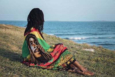 Woman sitting on shore at beach against sky