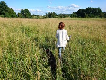 Rear view of woman with dog walking on grassy field