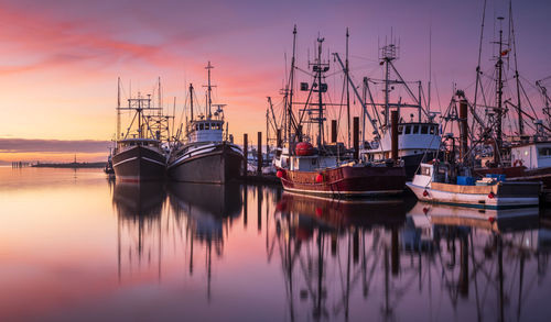 Sailboats moored at harbor against sky during sunset