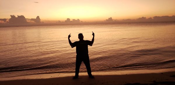 Rear view of silhouette man standing at beach during sunset