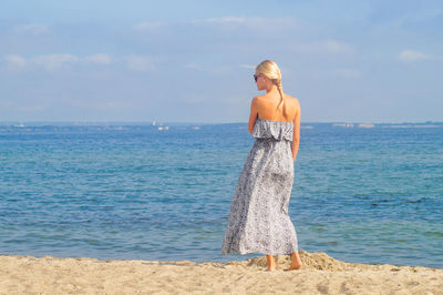 Rear view full length of young woman standing at sandy beach