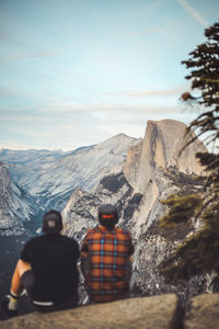 Two people sitting on rock ledge enjoying the view of half dome