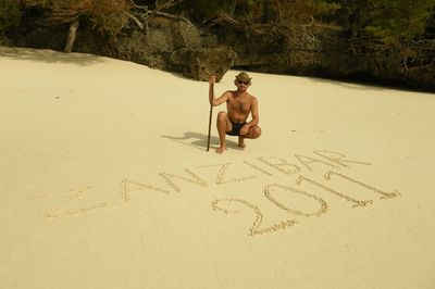 Full length of shirtless man with text in sand at beach